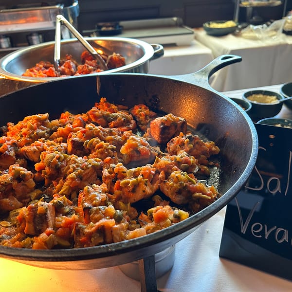 A cast iron skillet filled with Salmon Veracruz, featuring salmon pieces in a rich tomato and olive sauce.