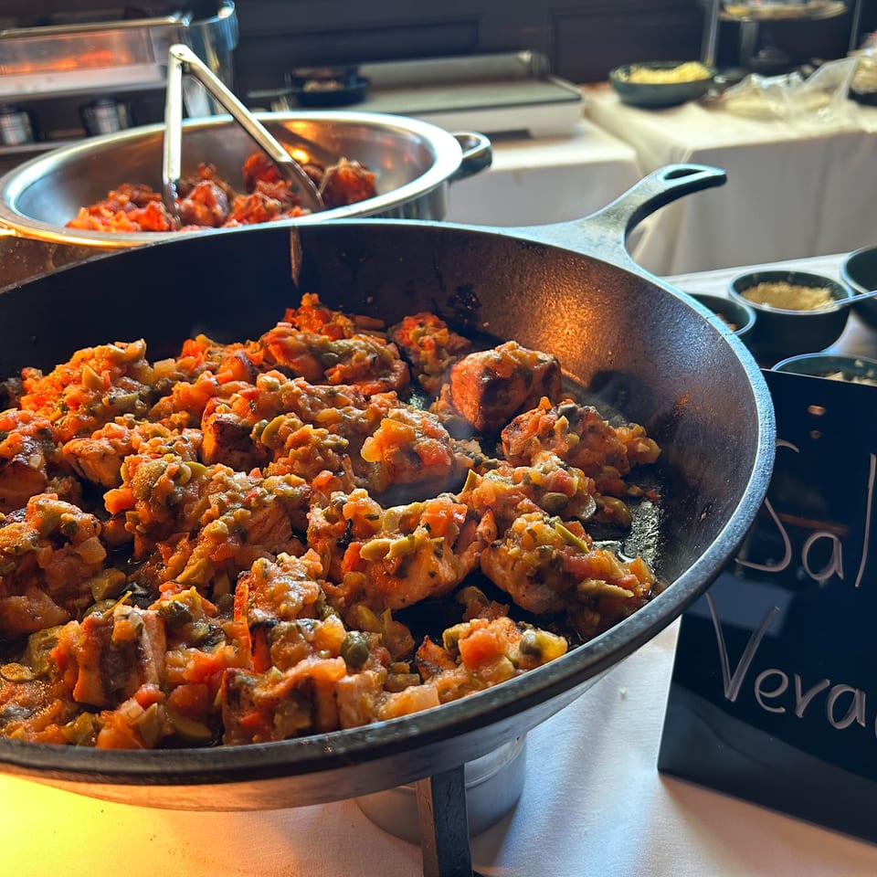A cast iron skillet filled with Salmon Veracruz, featuring salmon pieces in a rich tomato and olive sauce.