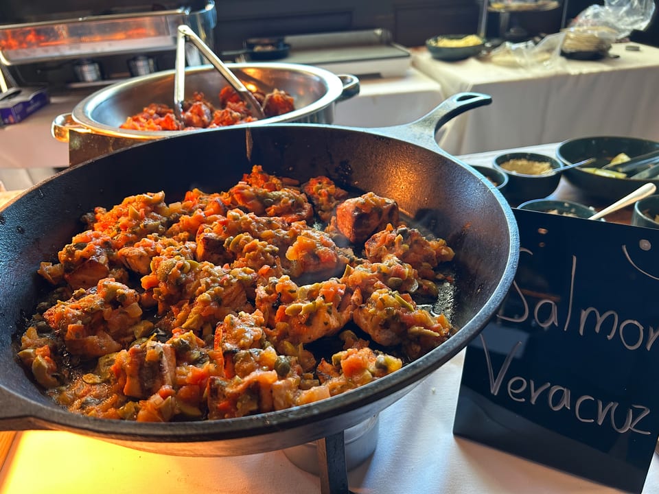 A cast iron skillet filled with Salmon Veracruz, featuring salmon pieces in a rich tomato and olive sauce.