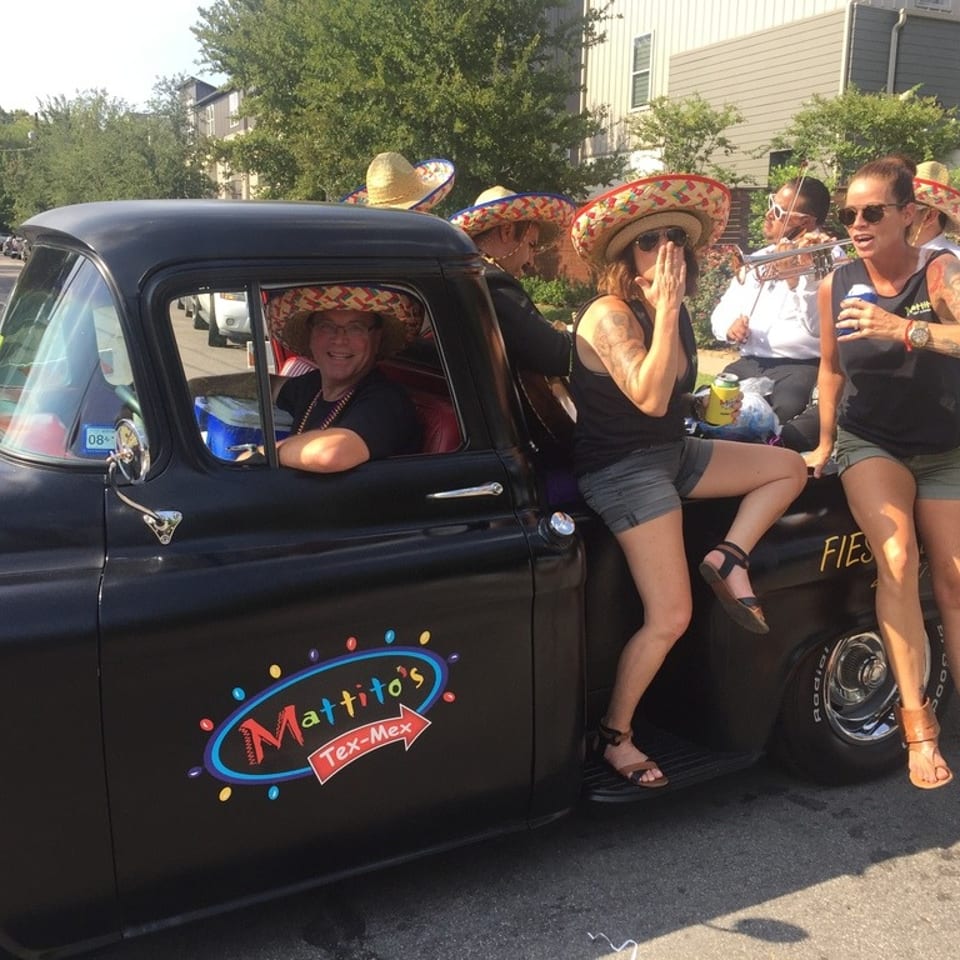 People in sombreros on a black Mattito's Tex-Mex truck, with one person driving and others in the back.