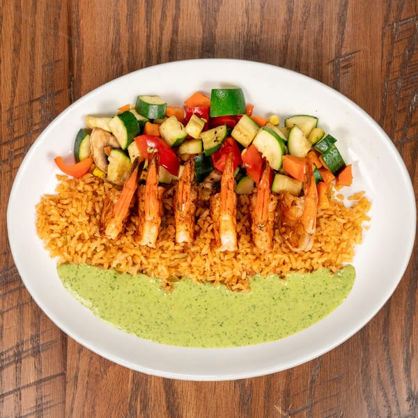 Grilled shrimp with rice, mixed vegetables, and a green sauce on a white plate.