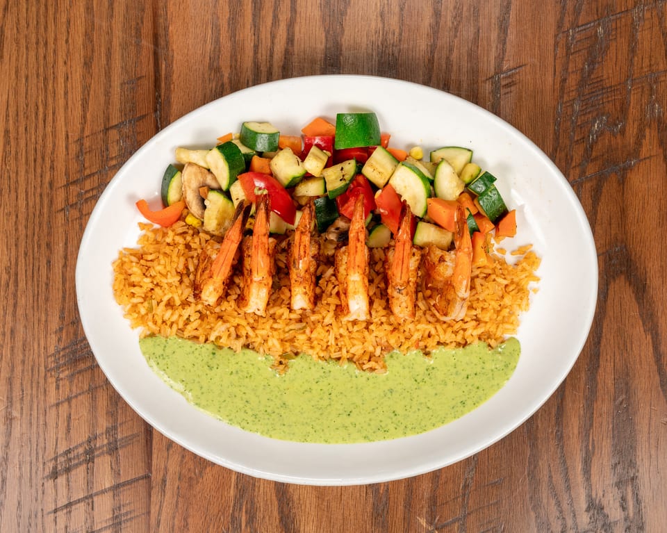 Grilled shrimp with rice, mixed vegetables, and a green sauce on a white plate.