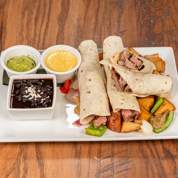 Steak fajita wraps with roasted vegetables, black beans, guacamole, and cheese sauce on a white plate.