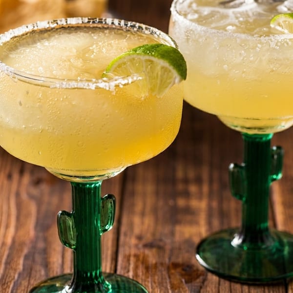 Two frosty margaritas in cactus-stemmed glasses with lime wedges, salt rims, and tortilla chips.