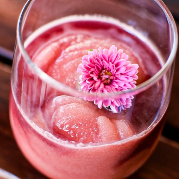 Close-up of a pink frozen drink in a glass, garnished with a vibrant pink flower.
