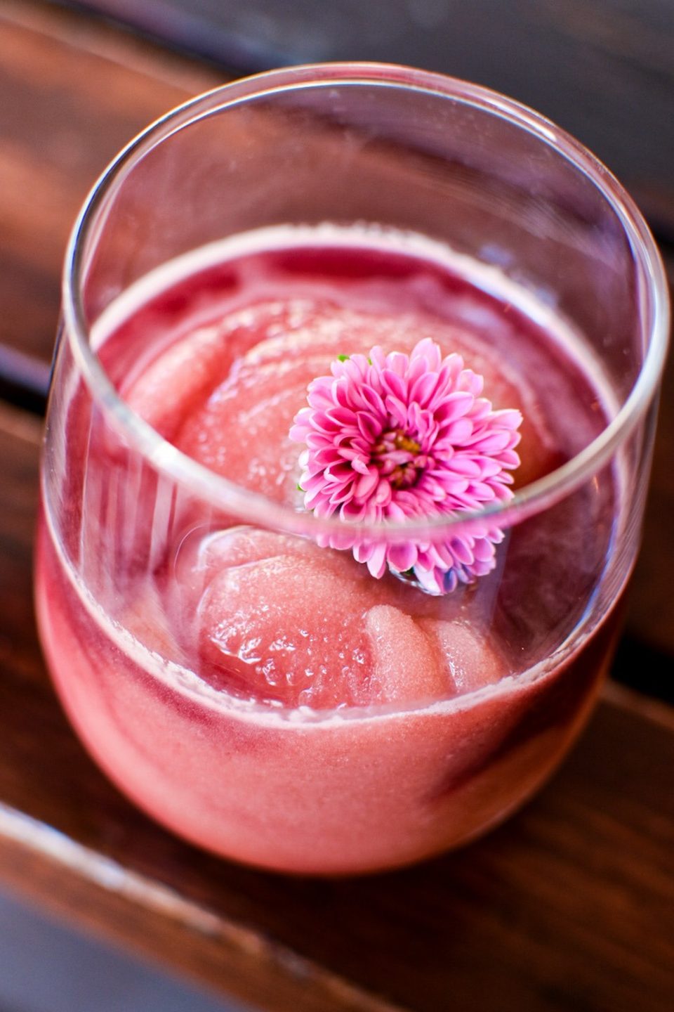 Close-up of a pink frozen drink in a glass, garnished with a vibrant pink flower.