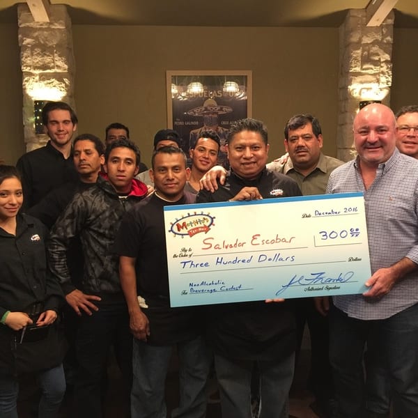 A group of restaurant staff and managers holding a large check for $300 to Salvador Escobar.