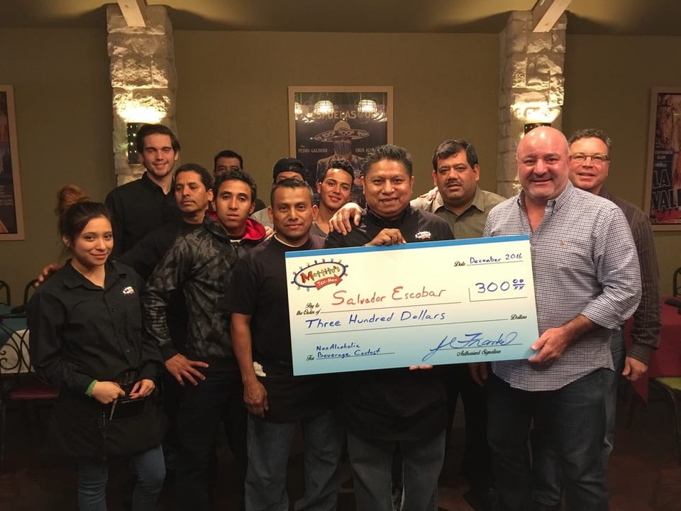 A group of restaurant staff and managers holding a large check for $300 to Salvador Escobar.
