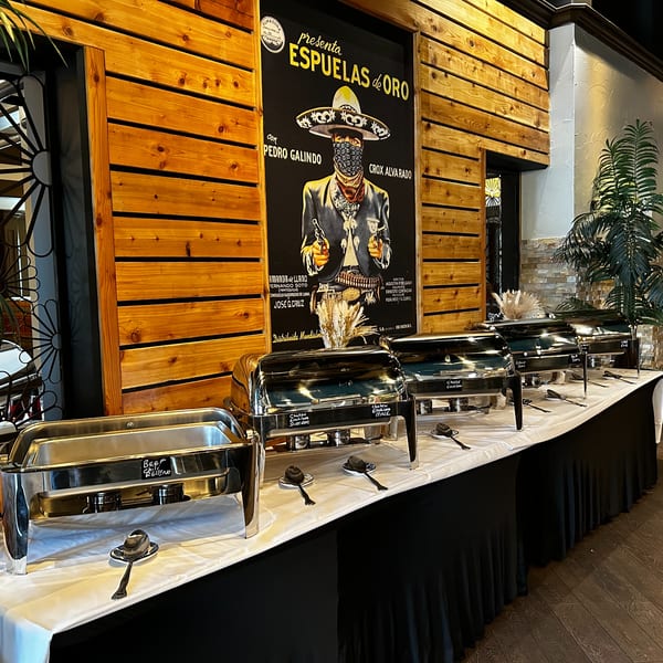 Buffet table with several chafing dishes, a large poster, and wooden wall paneling in a restaurant.