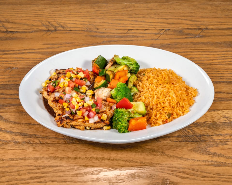 Grilled chicken with corn salsa, mixed vegetables, and Spanish rice on a white plate.
