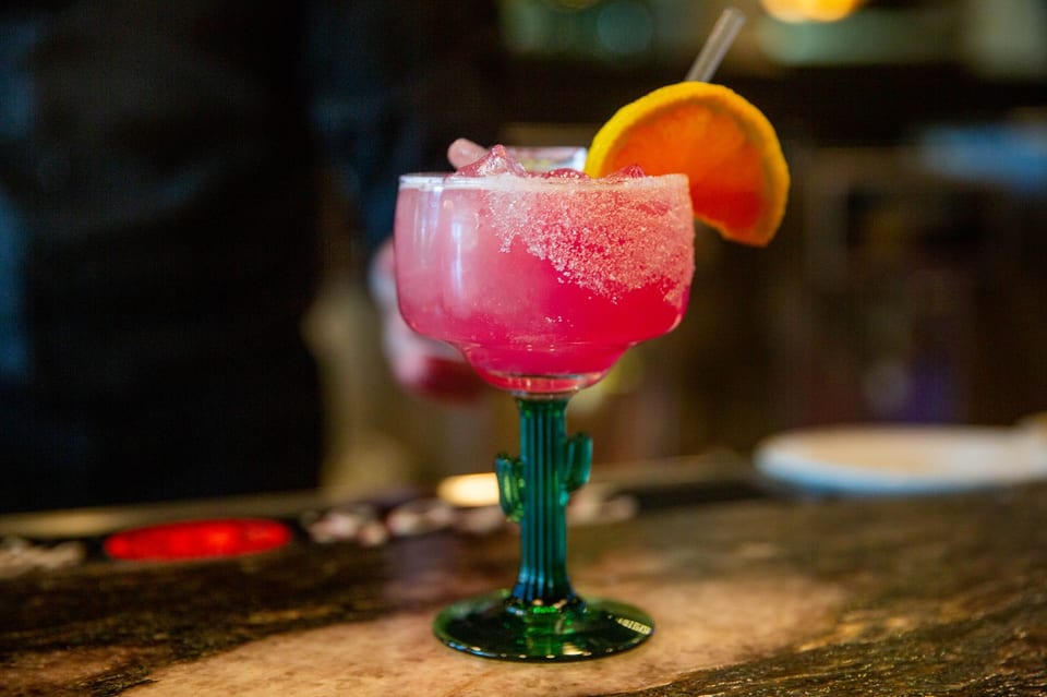 A vibrant pink margarita in a cactus-stemmed glass, garnished with an orange slice and straw.