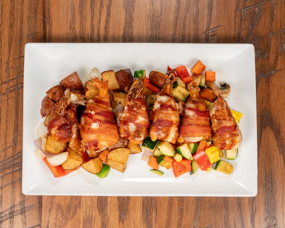 Bacon-wrapped shrimp with roasted potatoes and mixed vegetables on a white rectangular plate.