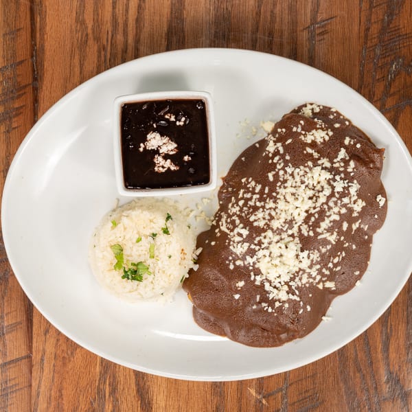 A plate of chicken mole with rice and black beans, garnished with cheese and cilantro.