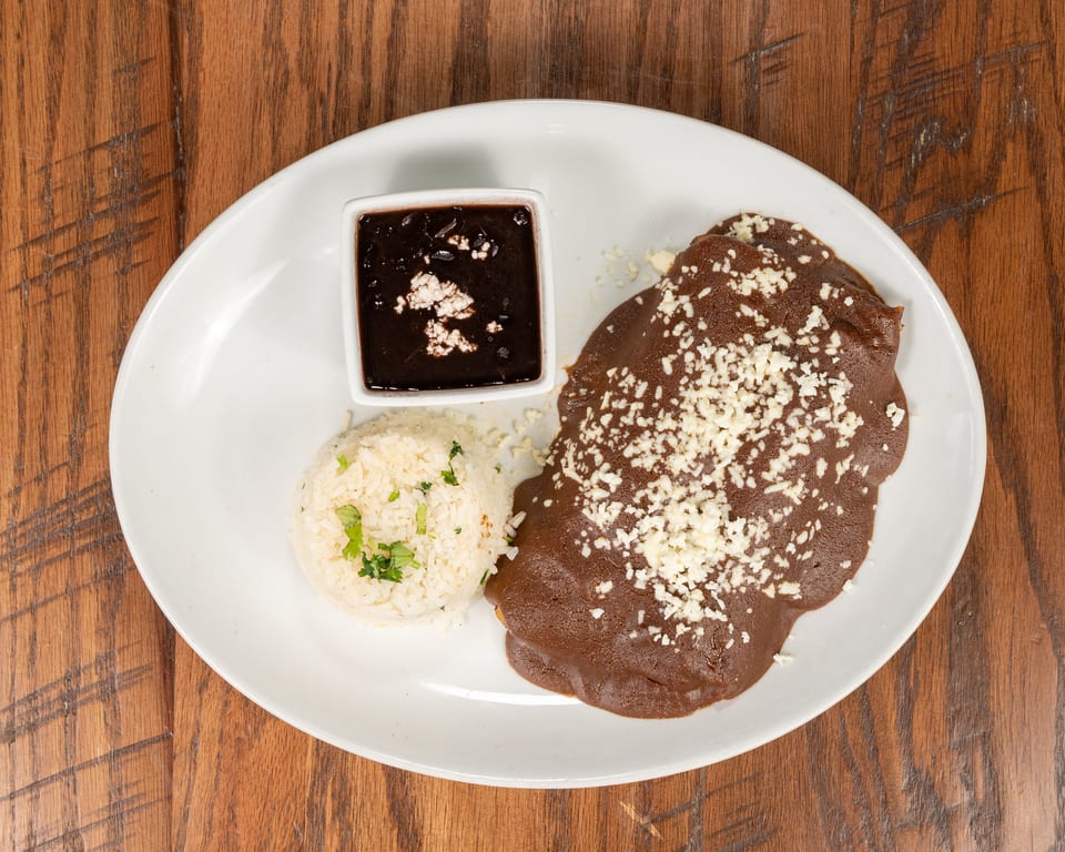 A plate of chicken mole with rice and black beans, garnished with cheese and cilantro.