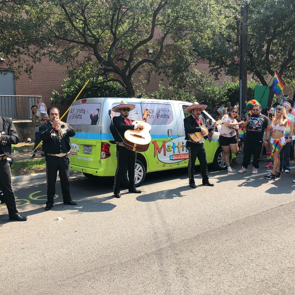 Mariachi band performing in front of a Mattitos van for a crowd of people at a parade.