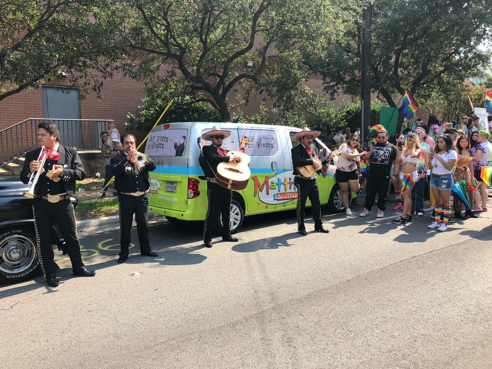 Mariachi band performing in front of a Mattitos van for a crowd of people at a parade.