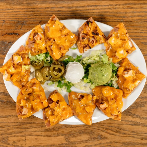 Chicken nachos with melted cheese, lettuce, jalapeños, sour cream, and guacamole on a white plate.