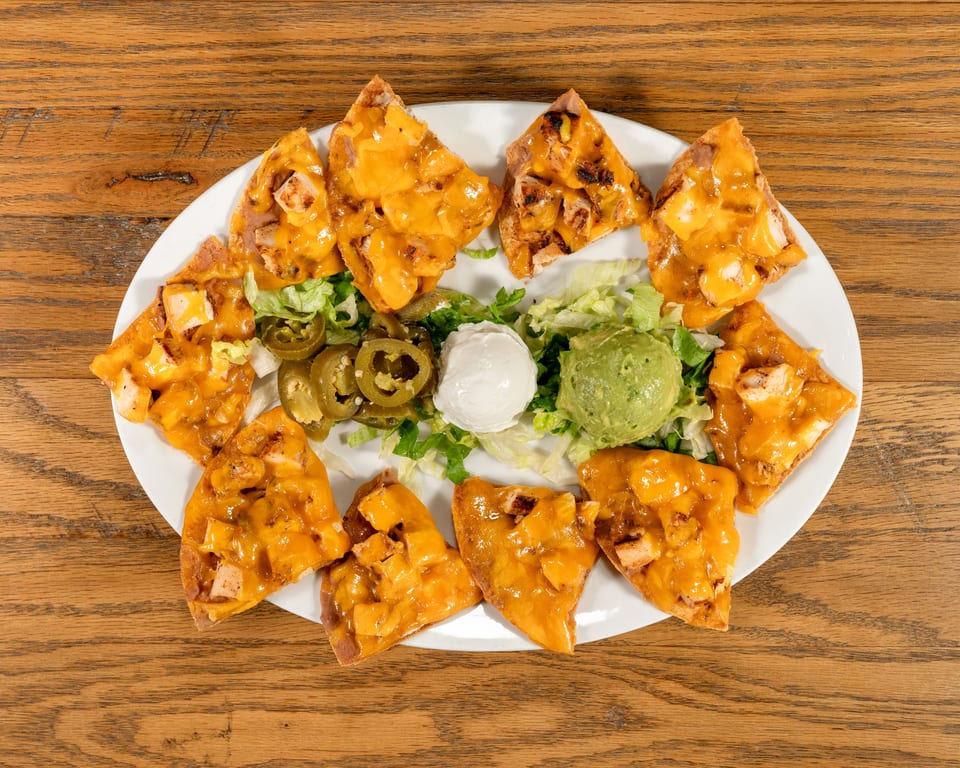 Chicken nachos with melted cheese, lettuce, jalapeños, sour cream, and guacamole on a white plate.