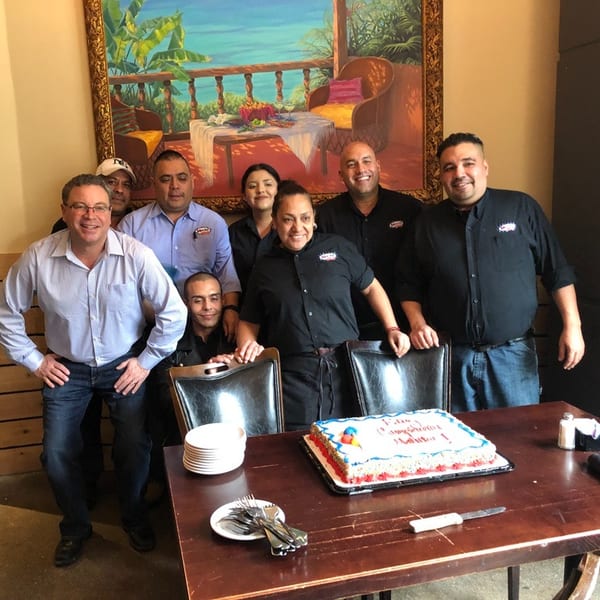Restaurant staff gathered around a table with a birthday cake, smiling at the camera.
