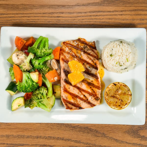 Grilled salmon with orange slices, roasted vegetables, rice, and a grilled lemon on a white plate.