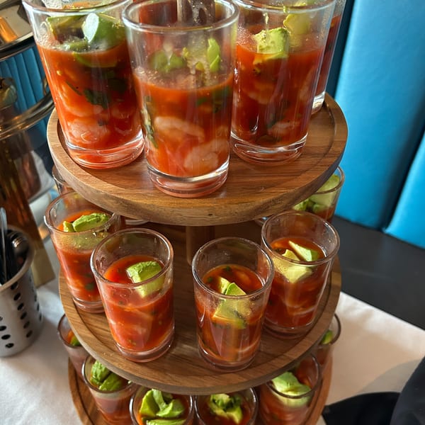 Shrimp cocktail shooters with avocado on a three-tiered wooden stand, with a blue booth in the background.