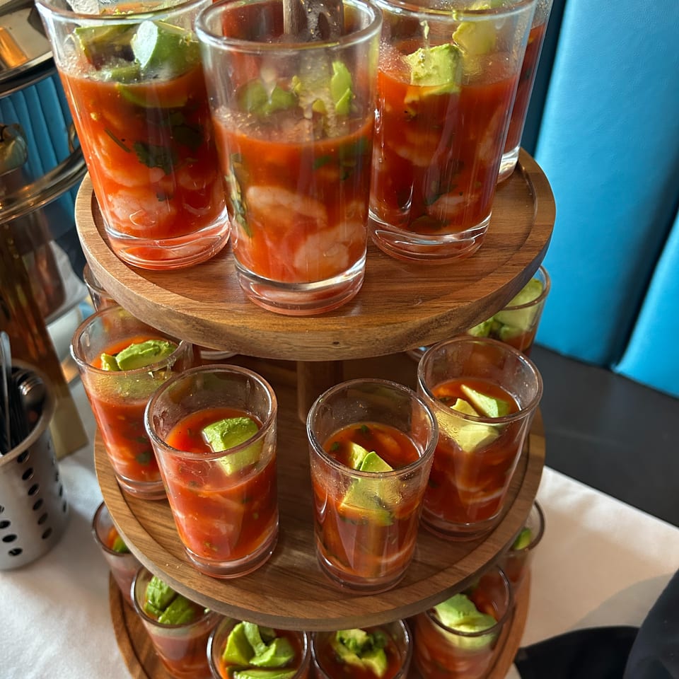Shrimp cocktail shooters with avocado on a three-tiered wooden stand, with a blue booth in the background.