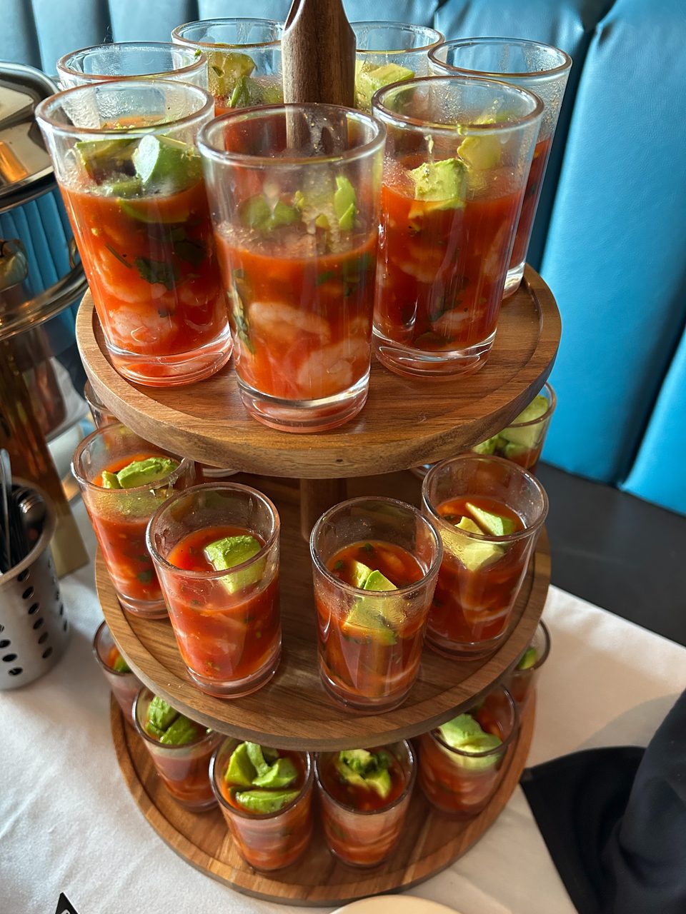Shrimp cocktail shooters with avocado on a three-tiered wooden stand, with a blue booth in the background.