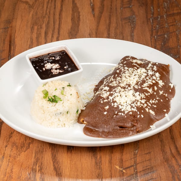A plate of enchiladas with mole sauce and cheese, served with rice and black beans.