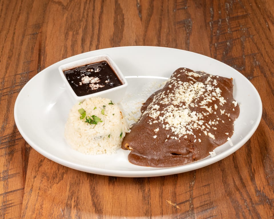 A plate of enchiladas with mole sauce and cheese, served with rice and black beans.