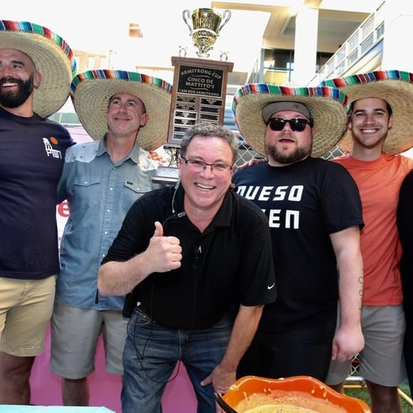 Six men in sombreros pose with a trophy and a bowl of queso at an outdoor event.