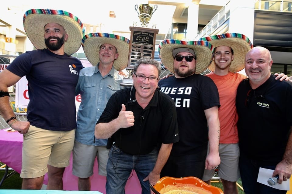 Six men in sombreros pose with a trophy and a bowl of queso at an outdoor event.