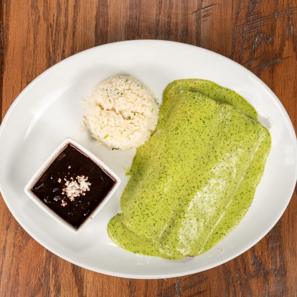 A plate of green enchiladas with rice and a side of black beans on a wooden table.