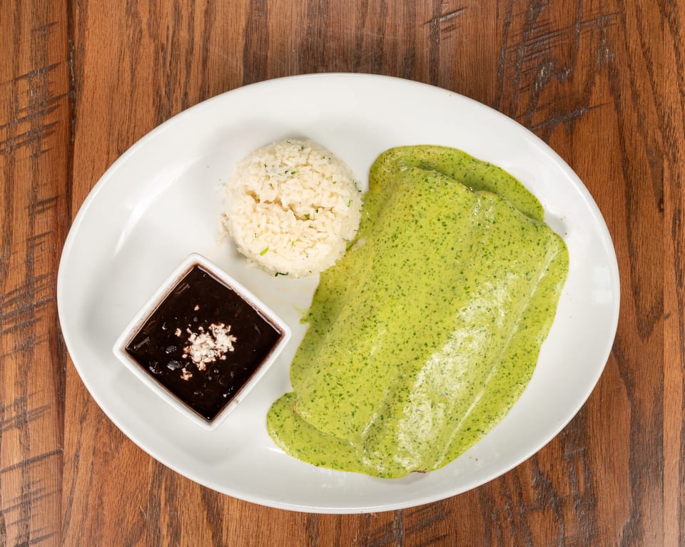 A plate of green enchiladas with rice and a side of black beans on a wooden table.