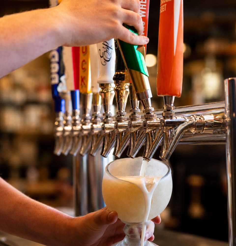 A bartender pours a frothy, light-colored drink from a tap into a glass.