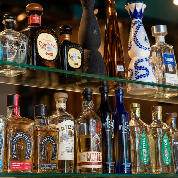 Two shelves filled with various brands of tequila and mezcal bottles, including Don Julio and Herradura.