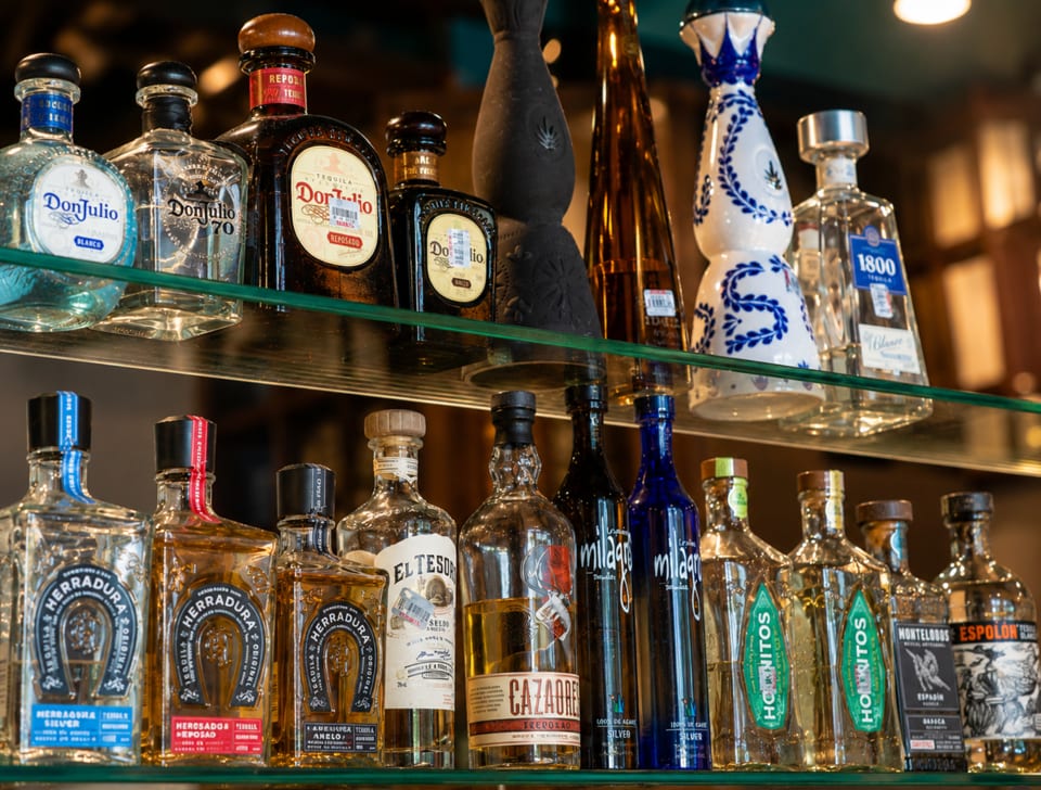 Two shelves filled with various brands of tequila and mezcal bottles, including Don Julio and Herradura.