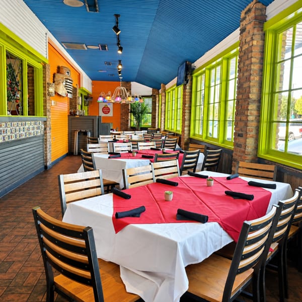 Vibrant restaurant interior with red and white tablecloths, wooden chairs, lime green window frames, and a blue ceiling.